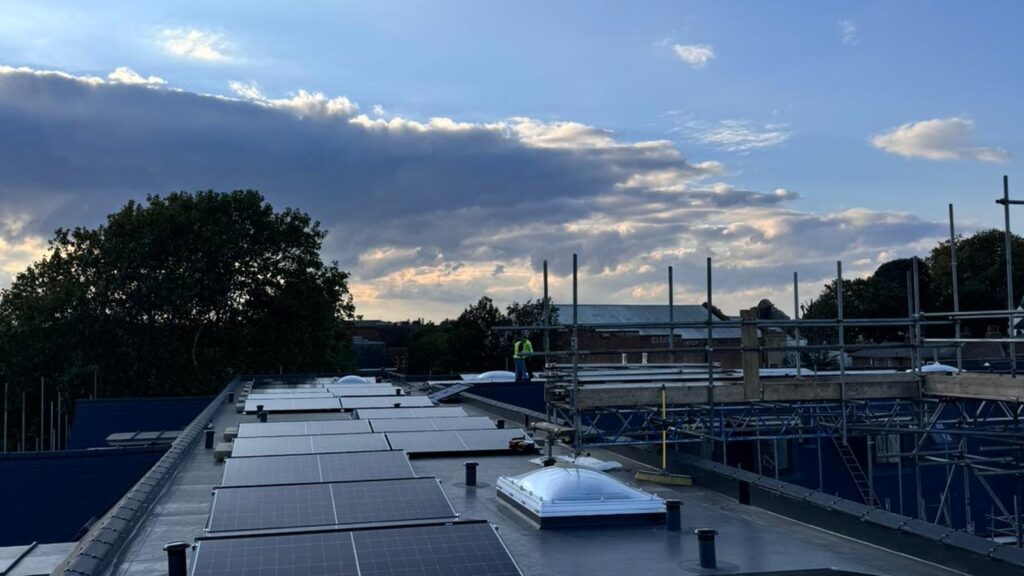 Completed rows of solar panels on a flat roof at dusk, with scaffolding at the edge