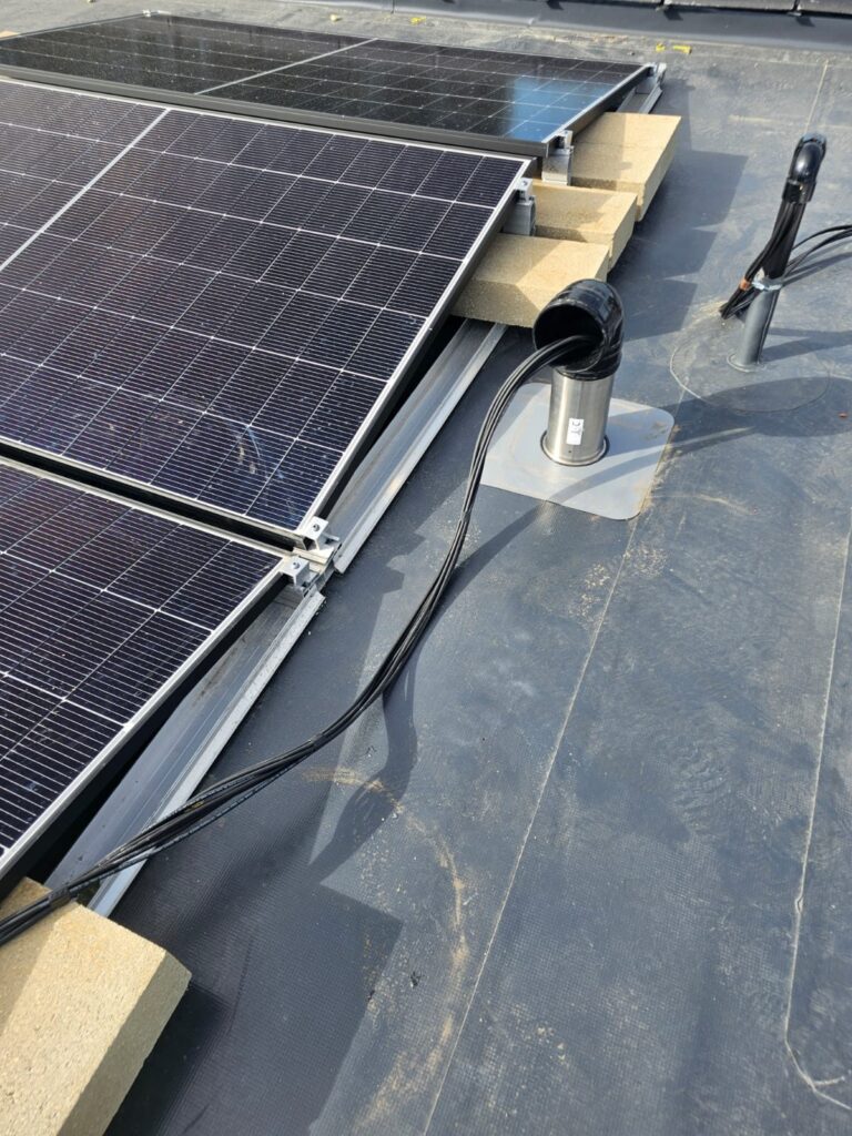 Close view of solar panels clamped to ballasted mounting frames with cabling run across the roof
